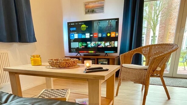 A cozy living room with a sofa, a TV, a table with a candle, and a wicker chair.