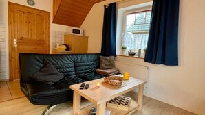 A cozy room with a black leather sofa, a wooden coffee table with a candle, a small basket, and a window with blue curtains.