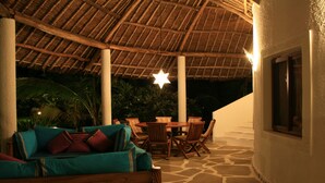 Uma área de pátio ao ar livre com telhado de palha, móveis de madeira e luminária em formato de estrela.