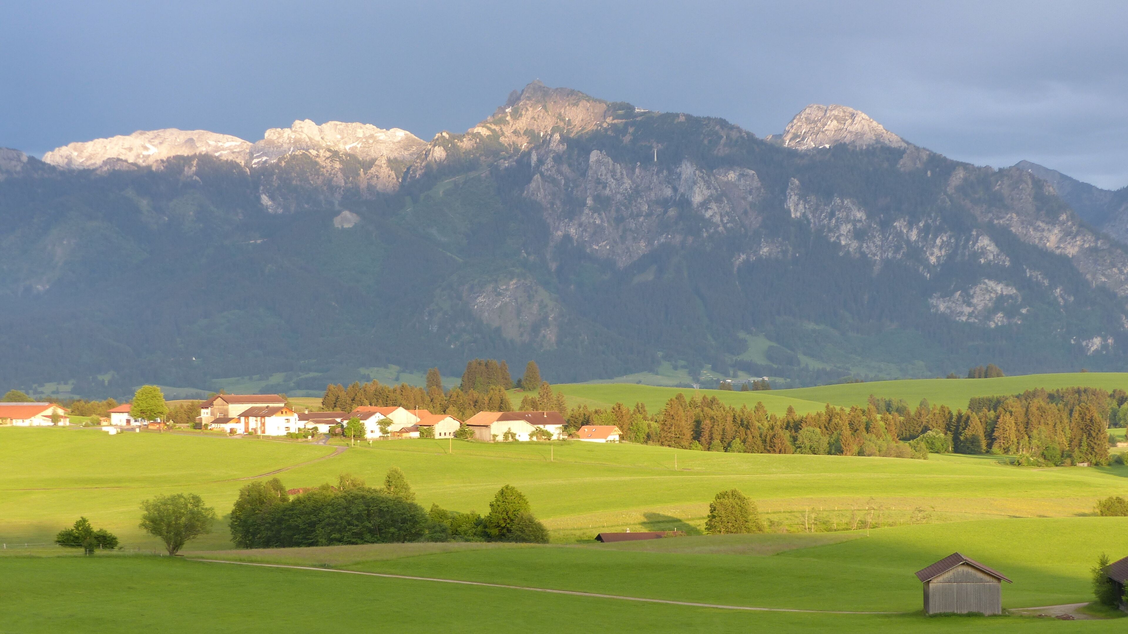 A rural landscape with a mountain range in the background, houses in the foreground, and a clear sky.