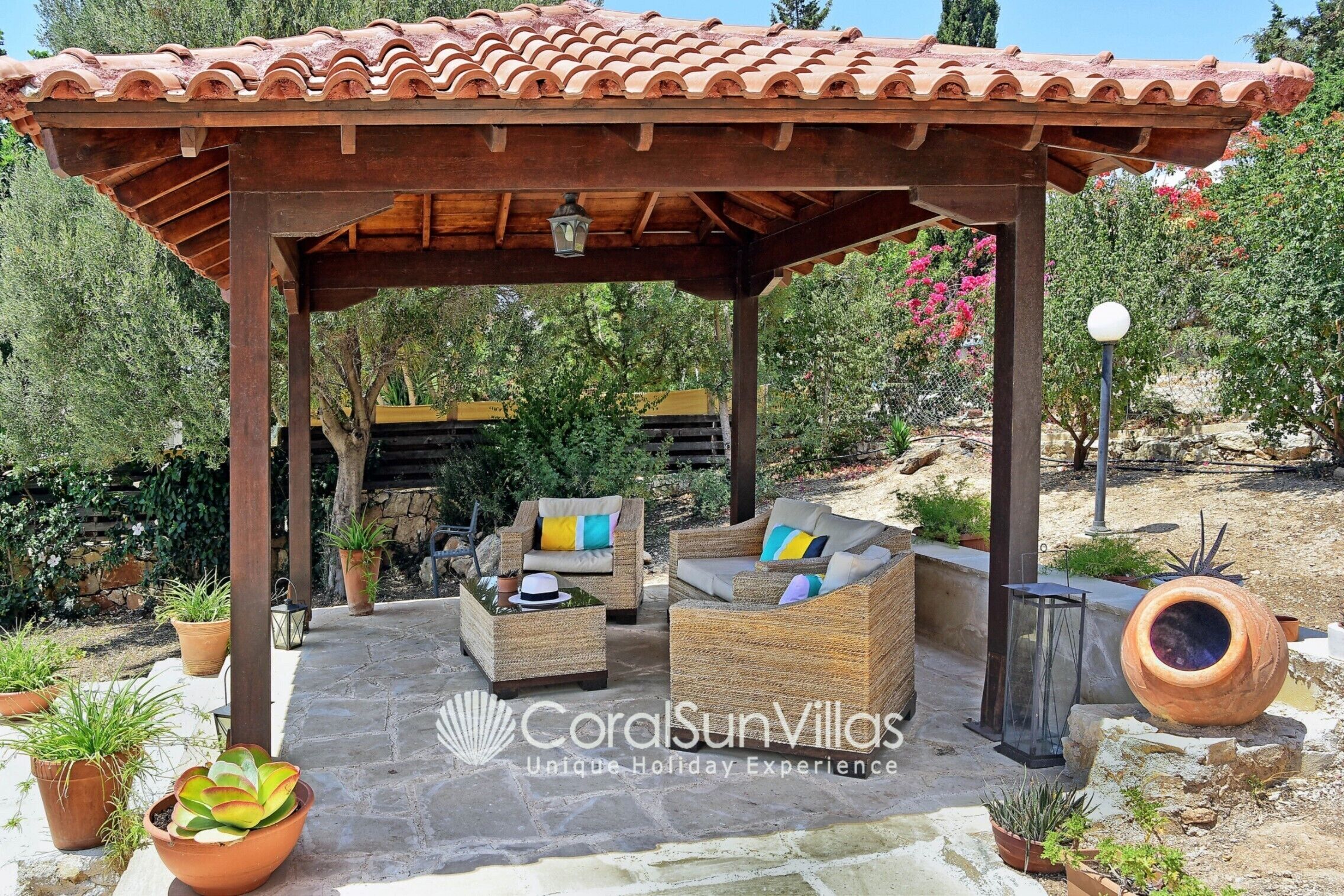 A covered outdoor seating area with wicker furniture, potted plants, and a stone floor.