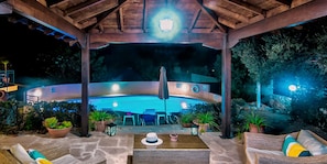 A covered outdoor pool area with lounge chairs and a table, surrounded by potted plants.