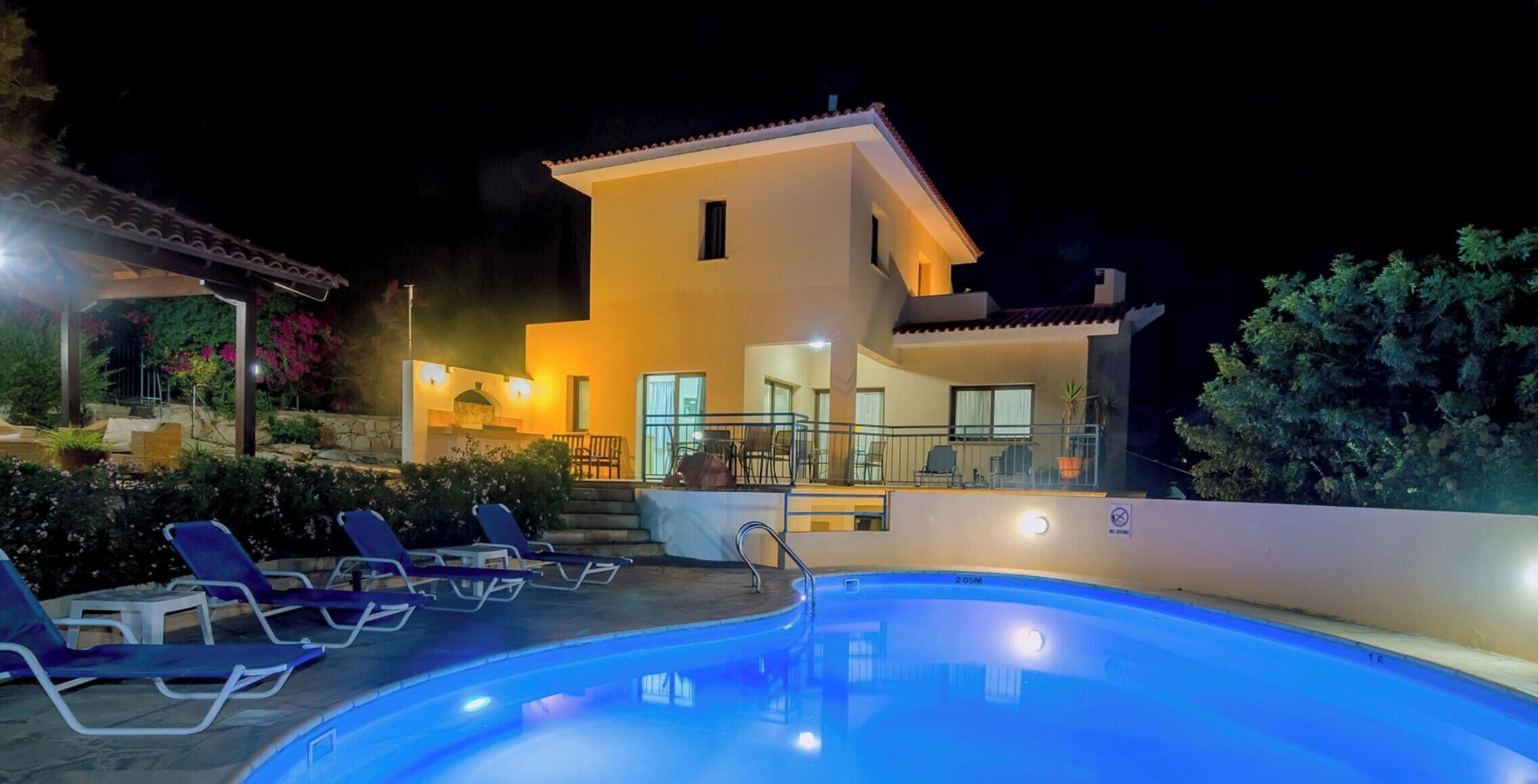 A two-story building with a swimming pool, outdoor seating, and a well-lit entrance.