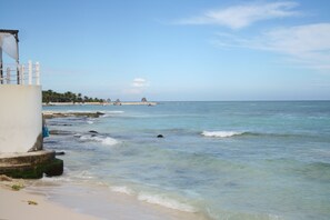 A beach with clear waters, a white building, and palm trees in the background. - Apartments Paraiso Maya 19-b (Puerto Morelos)