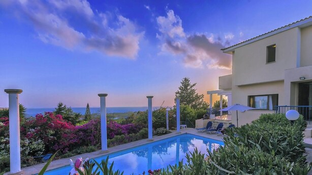 A swimming pool with lounge chairs, a building with a balcony, and a view of the sea. - Wonderful Quiet Area, Completely Privacy, Large Private Pool, Colourful Garden (Pegeia)