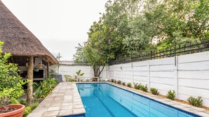 A swimming pool with a thatched roof structure, surrounded by a white fence and lush greenery. - Stylish 2-bed Apartment in Centurion, Pretoria (Centurion)