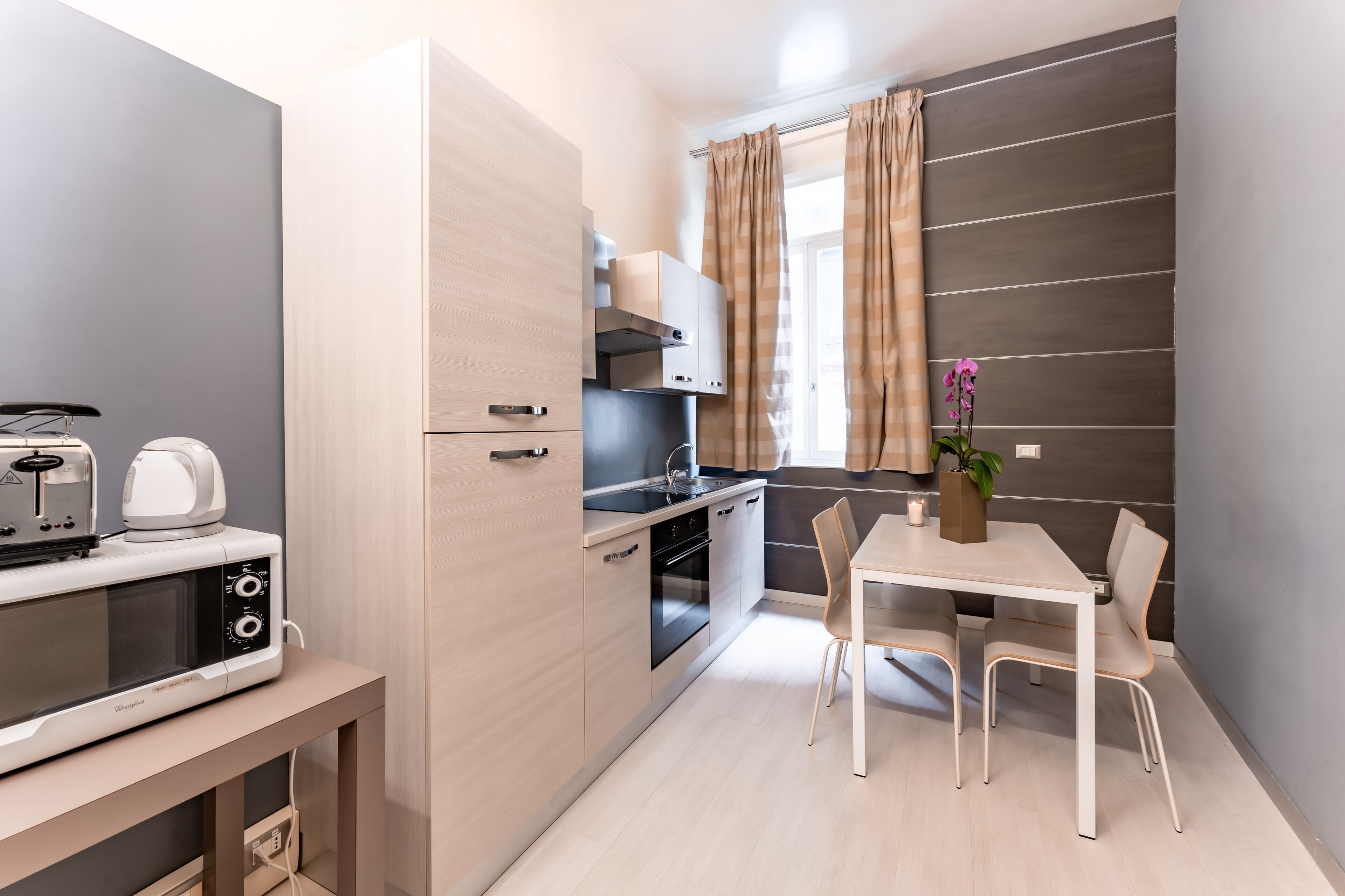 A compact kitchen with a microwave, toaster, and oven. There is a dining table with chairs and a potted plant.