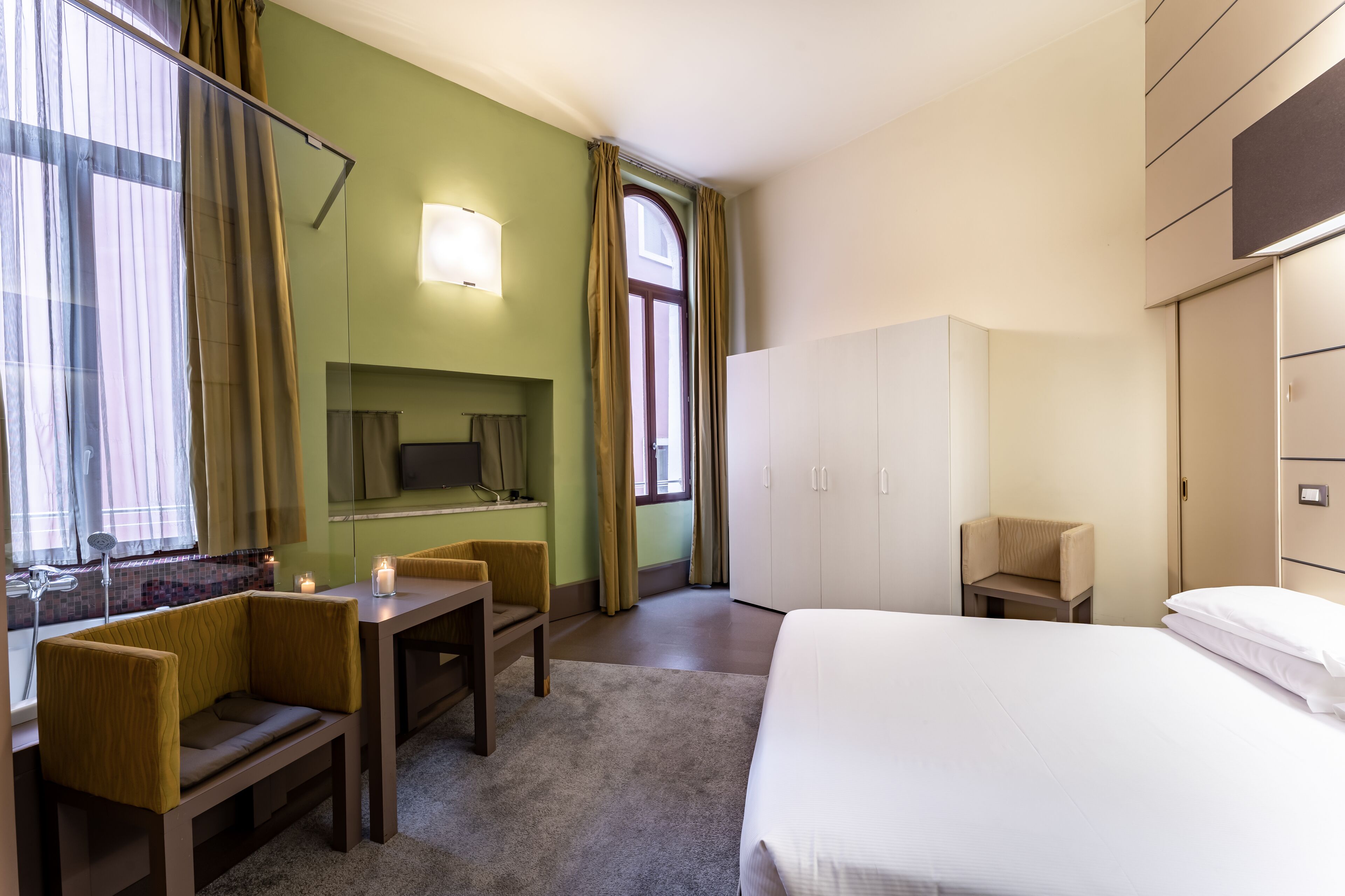 A hotel room with a bed, a desk, a chair, a TV, and a wardrobe.