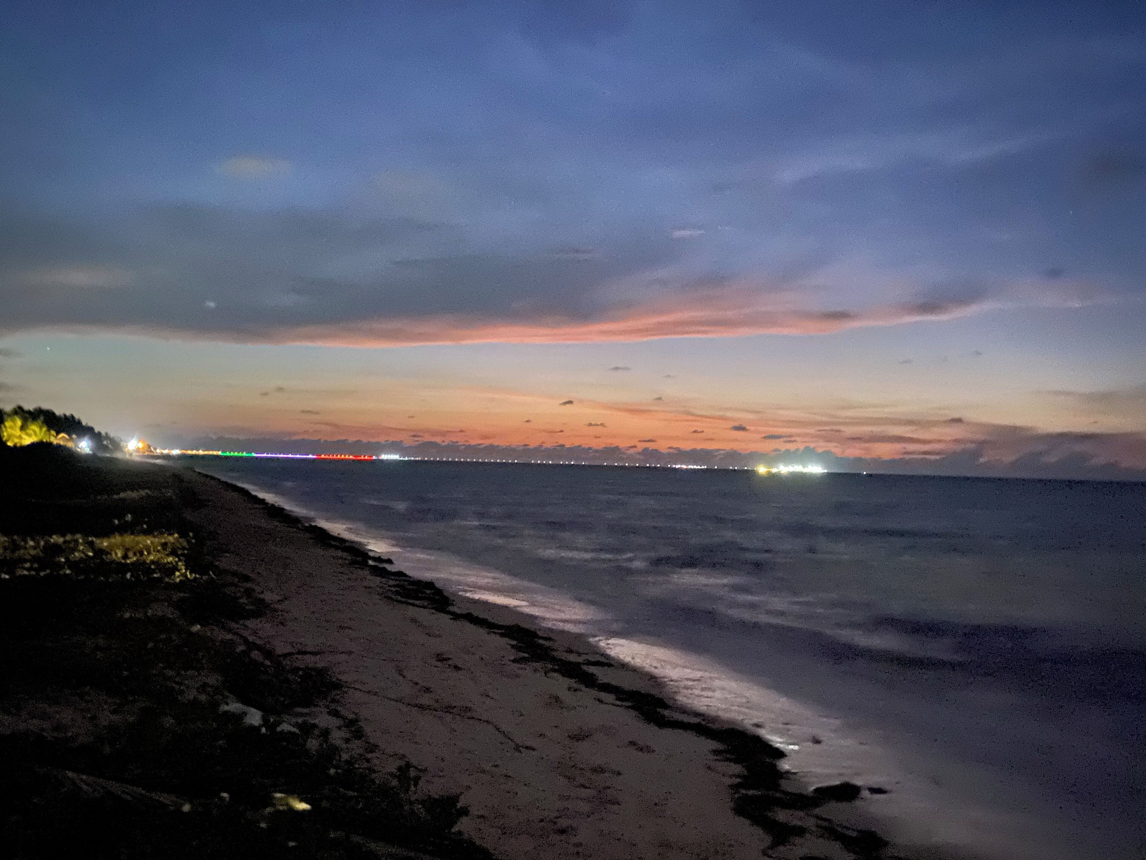 A beach at dusk with a distant cityscape and a bridge.