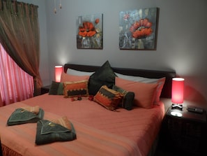 A neatly made bed with a striped bedspread, multiple pillows, and two bedside lamps. There are two paintings on the wall above the bed. - Family Apartment Bloemfontein Cherry Lane Self Catering and BB max 6 Guests (Bloemfontein)