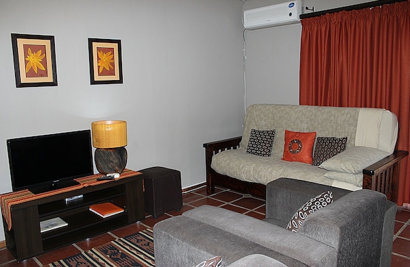 Una sala de estar con sofá, sillón, televisión y una lámpara sobre un pedestal.