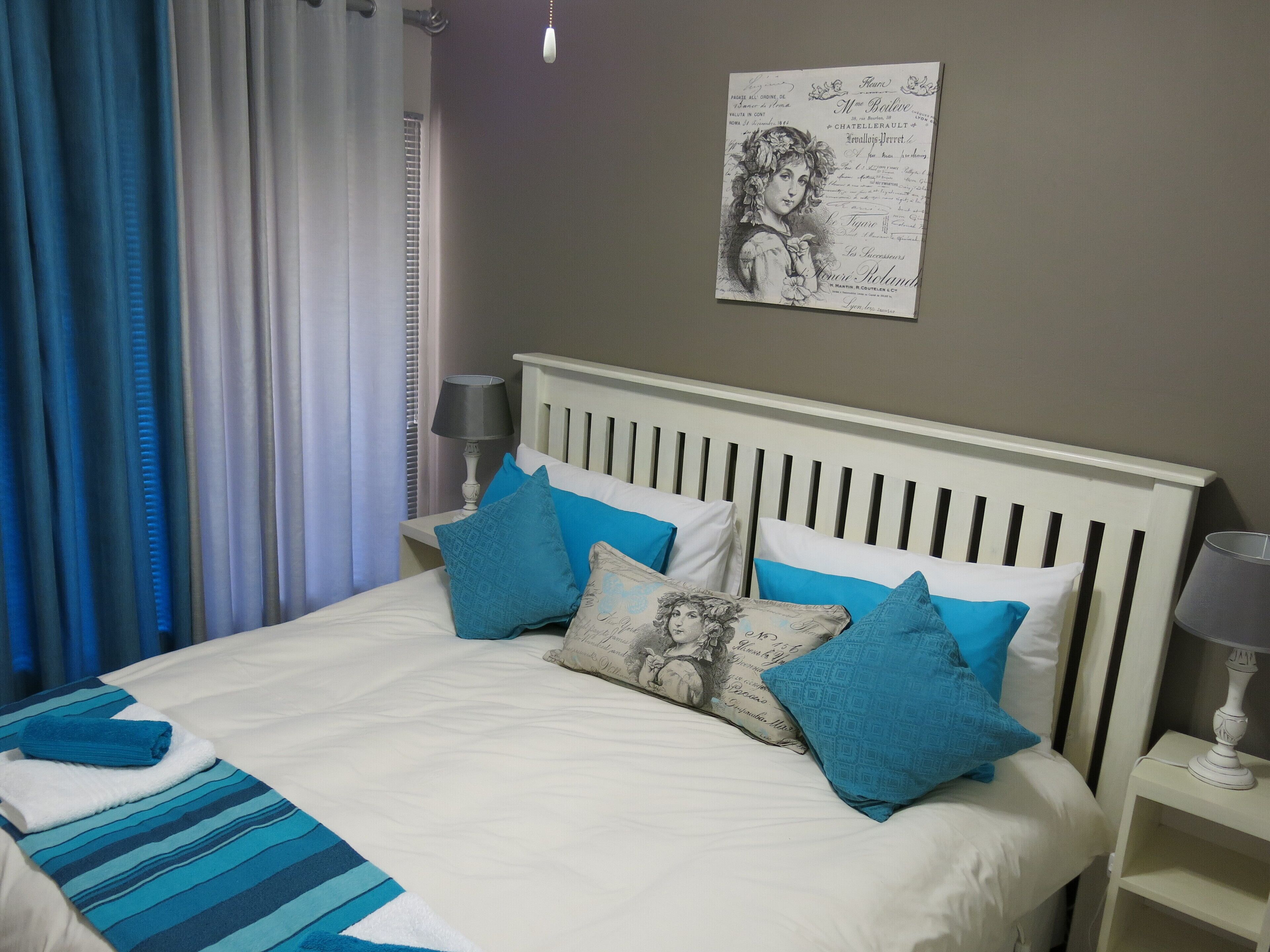 A neatly made bed with blue and white bedding, two bedside lamps, and a wall-mounted artwork.