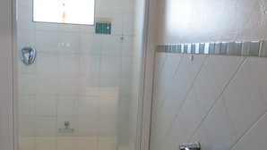 Ett badrum med en dusch som är avskärmad med glasväggar, vita kakelväggar och en handduksställning med två handdukar.