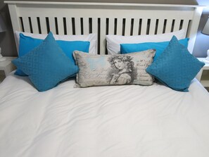 A bed with a white headboard, two blue pillows, and a central pillow with a printed design. - Cherry Lane Self Catering BB - 1 Bedroom Bathroom With Shower for 4 Guests (Bloemfontein)