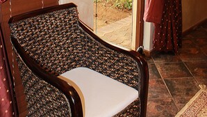 A wicker chair with a white cushion in a room with red curtains and a straw hat hanging on the wall. - Cherry Lane Self Catering and BB - Romantic Honeymoon Suite for 2 Bloemfontein (Bloemfontein)
