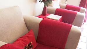 En beige sofa med røde puder og et rødt tæppe.