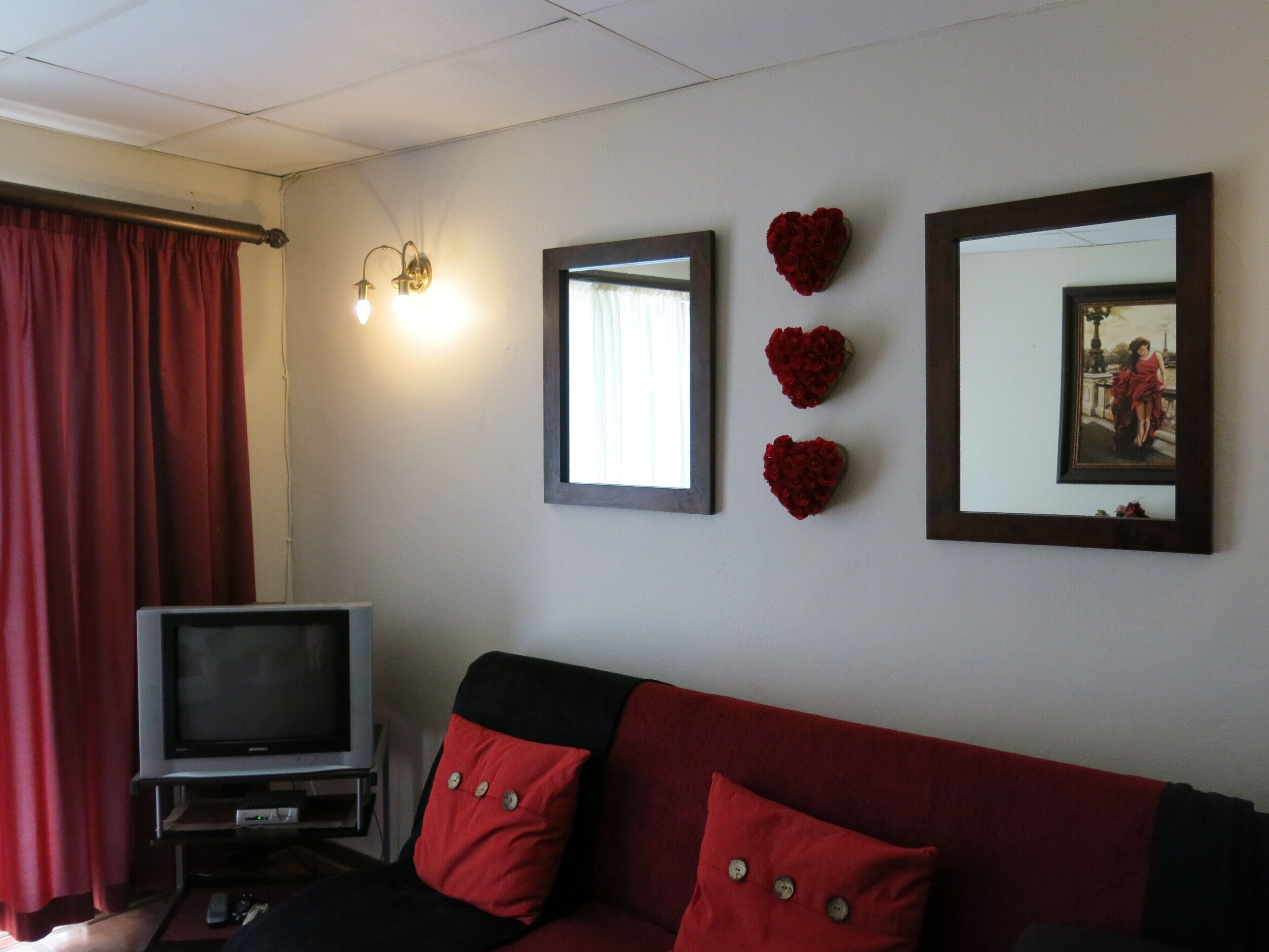 Un salon avec un canapé rouge, un téléviseur et des éléments de décoration fixés au mur, notamment des miroirs et des compositions florales en forme de cœur.