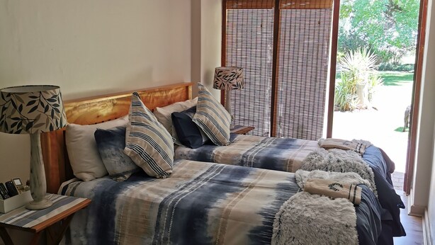 A bedroom with a large bed, a bedside table with a lamp, and a view of the outdoors through a window with blinds. - Cozy Triple Room With King Sized bed and Single Bed, Near Bloemfontein (Bloemfontein)
