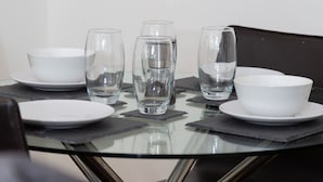 Une table à manger avec quatre bols blancs et trois verres transparents, posée sur une table en verre, avec une chaise noire en arrière-plan.