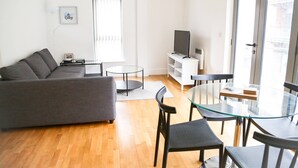 Una sala de estar moderna con un sofá gris, una mesa de centro de vidrio y un televisor sobre un mueble blanco.