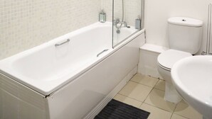 Moderni kylpyhuone, jossa on valkoinen kylpyamme, lasinen suihkuseinä, wc ja pesuallas.