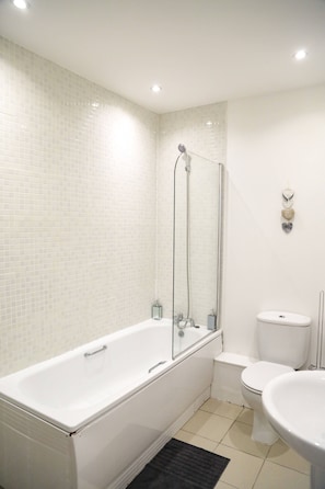 A modern bathroom with a white bathtub, a glass shower enclosure, a toilet, and a sink. - Henry Street - Apt 20 (Liverpool)