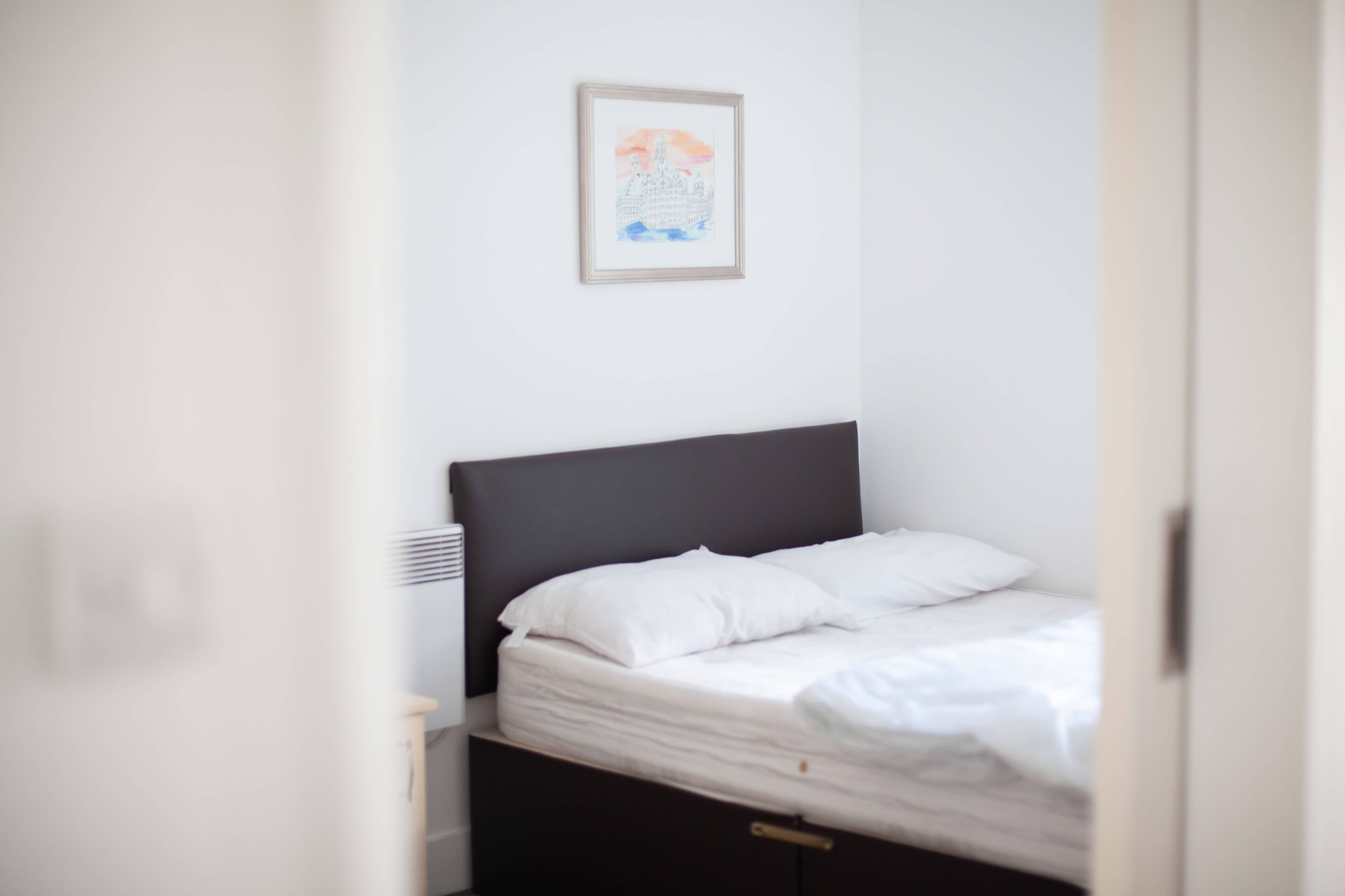 A bedroom with a bed, a headboard, a wall-mounted light, and a framed picture.