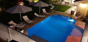 En rektangulär swimmingpool med blått kakel, omgiven av solstolar och parasoller.