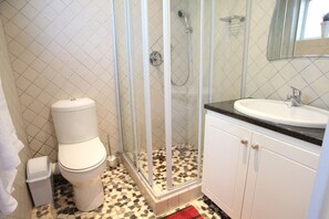 Une salle de bain comprenant des toilettes, une douche, un lavabo et un sol carrelé.