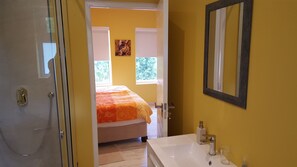 Ein Badezimmer mit Dusche, Waschbecken und einem Bett, das durch eine offene Tür sichtbar ist.