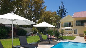 A swimming pool area with lounge chairs and umbrellas, surrounded by a well-maintained lawn and a house in the background.