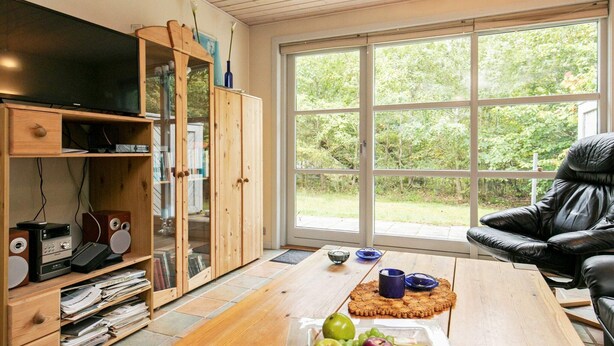 A living room with a wooden cabinet, a television, a leather chair, and a table with fruit. - Cozy Holiday Home in Hurup near Limfjorden (Hurup Thy)
