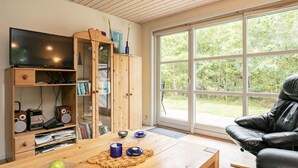 A living room with a wooden cabinet, a television, a leather sofa, and a large window. - Cozy Holiday Home in Hurup near Limfjorden (Hurup Thy)