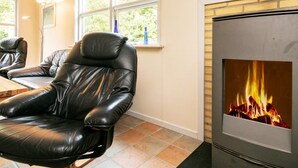 A room with a leather chair, a fireplace, and a window with a view of trees. - Cozy Holiday Home in Hurup near Limfjorden (Hurup Thy)