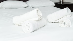 A neatly made bed with white linens and rolled towels, a dark headboard, a bedside table with a lamp, and a framed artwork of birds on the wall. - Henry Street - Apt 47 (Liverpool)