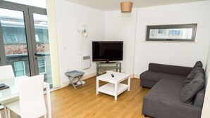 A modern living room with a grey sofa, white TV stand, and a dining table with chairs. - Henry Street - Apt 47 (Liverpool)