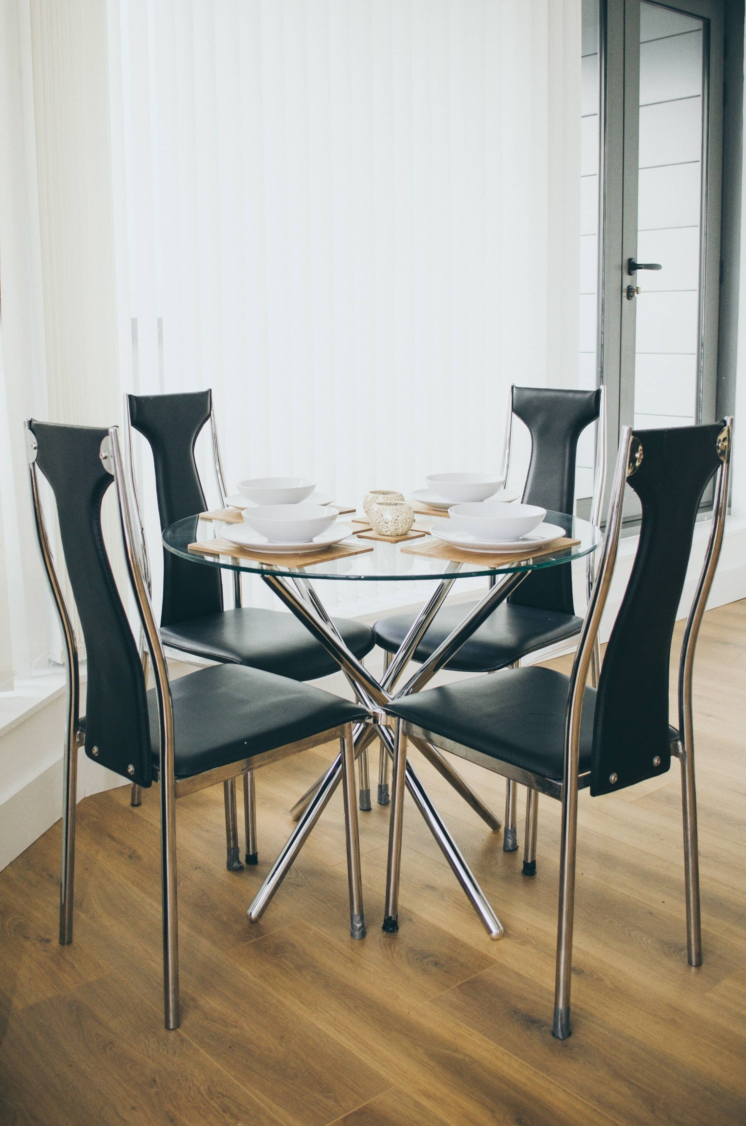 A round glass table with four black chairs, each with a metallic base.