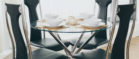 A round glass table with four black chairs, each with a metallic base.
