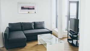 A modern living room with a grey sectional sofa, a glass coffee table, and a black entertainment unit with a TV. - Kent Street - Apt 15 (Liverpool)