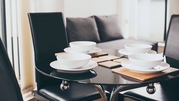 A dining table with white bowls and plates, surrounded by black chairs, in a modern room with a sofa and a window. - Kent Street - Apt 15 (Liverpool)