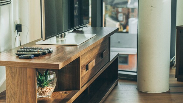 A modern living room with a wooden entertainment center, a flat-screen TV, and a view of a cityscape through large windows. - Kent Street - Apt 16 (Liverpool)
