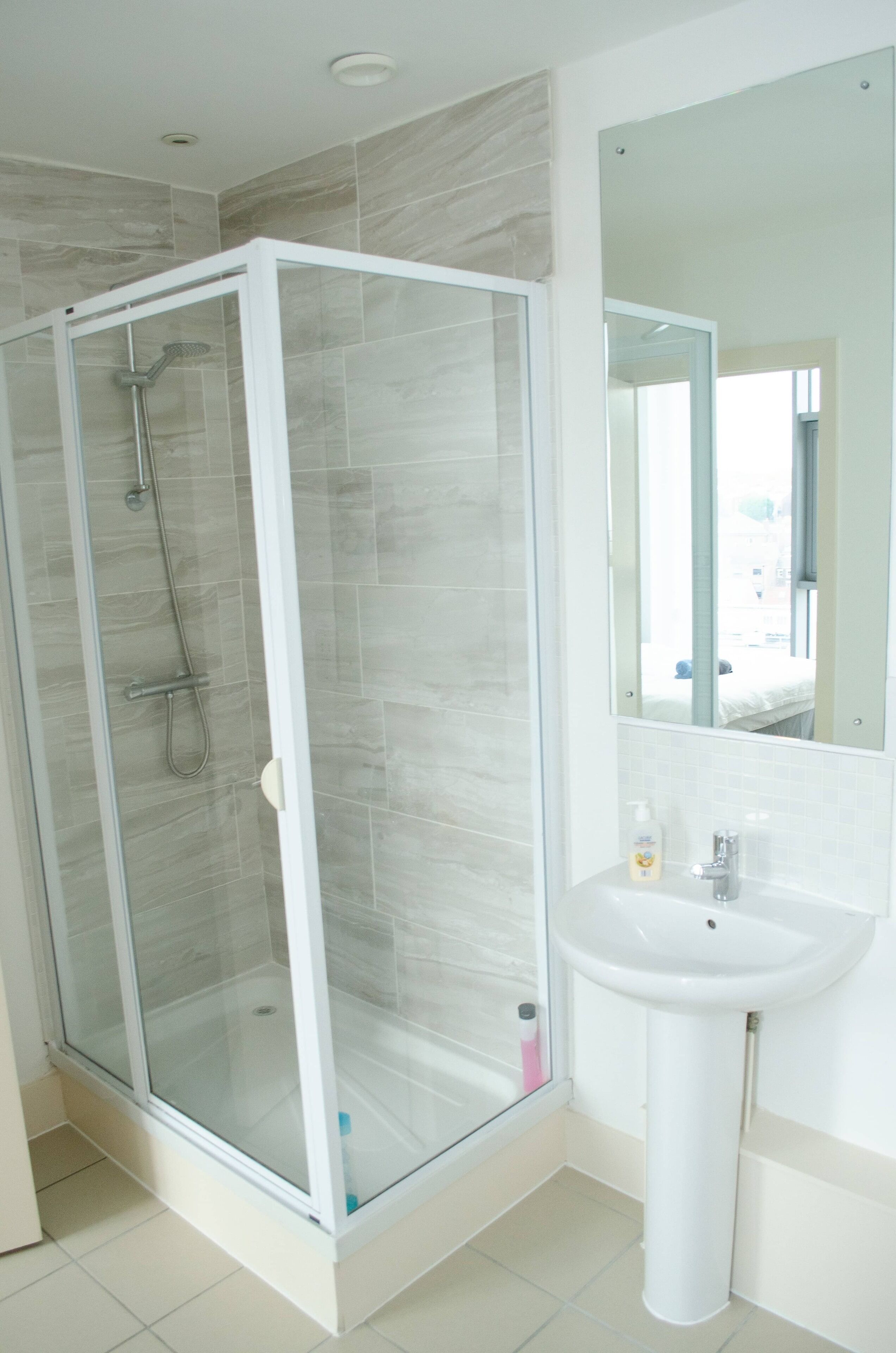 A modern bathroom with a glass-enclosed shower, a pedestal sink, and a large mirror.