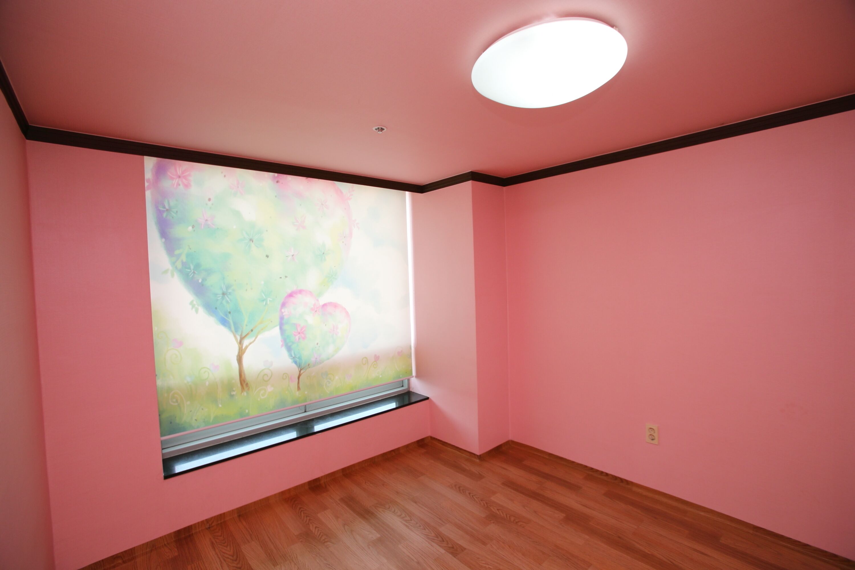 A room with pink walls, a wooden floor, and a large window with a painting of a tree and heart.