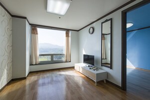 Una habitación con un ventanal grande, un televisor de pantalla plana, una mesita de noche y un espejo en la pared.