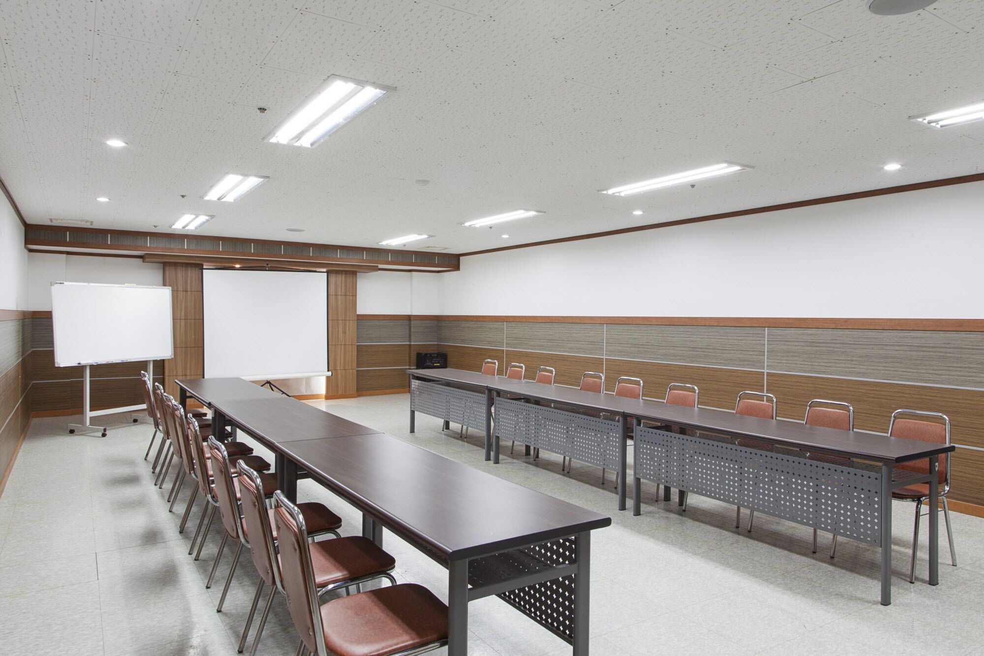 A conference room with a long table, chairs, a whiteboard, and a projector screen.