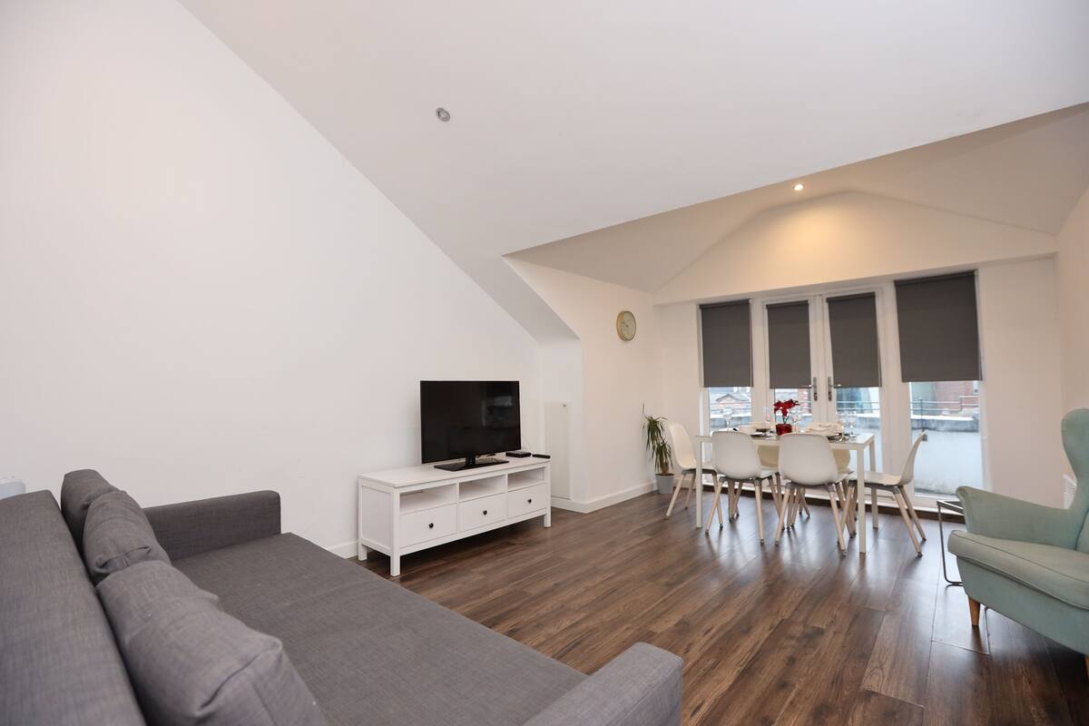 A modern living room with a grey sofa, a white entertainment unit, and a dining area with a table and chairs.