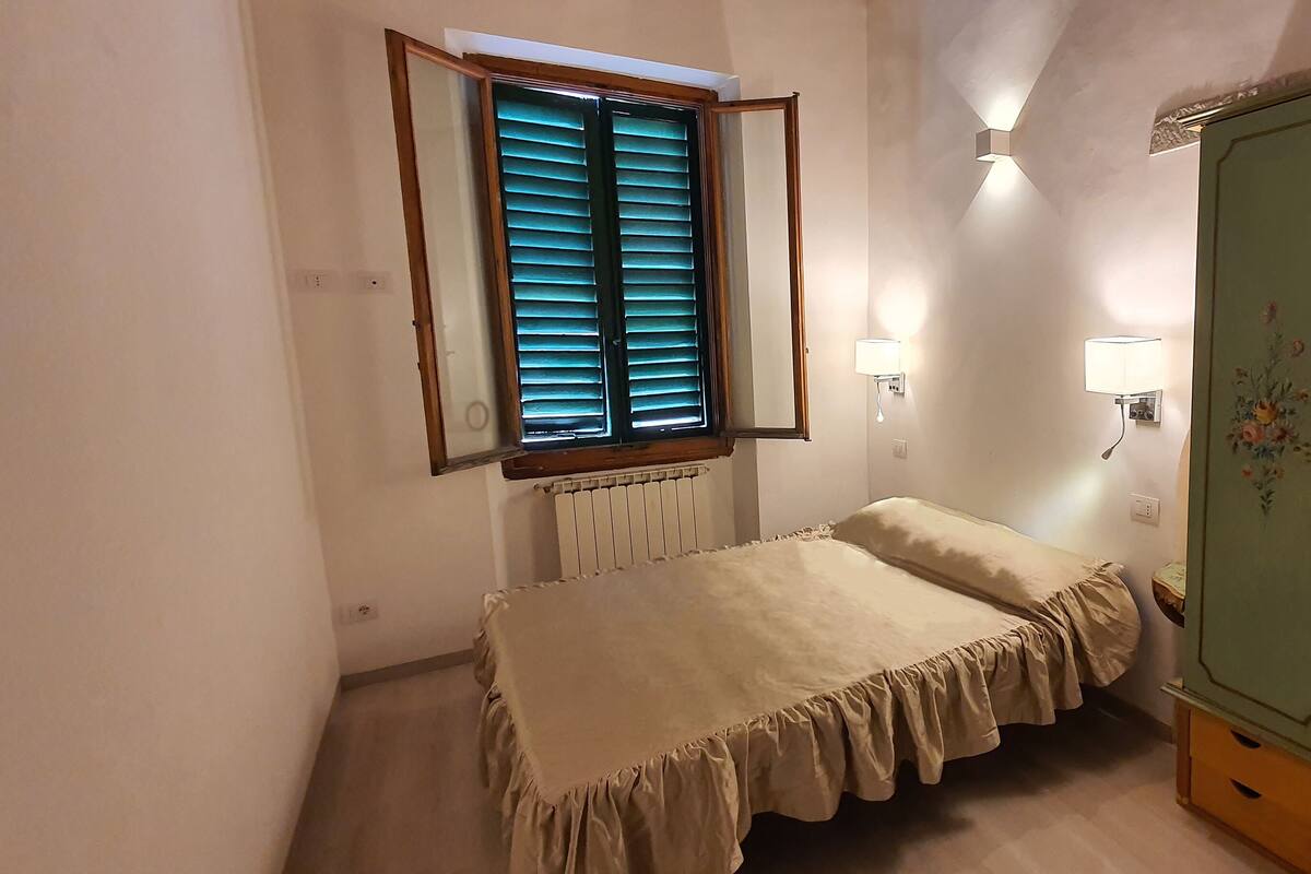 A small bedroom with a single bed, a radiator, a window with blinds, a wardrobe, and two wall-mounted lamps.