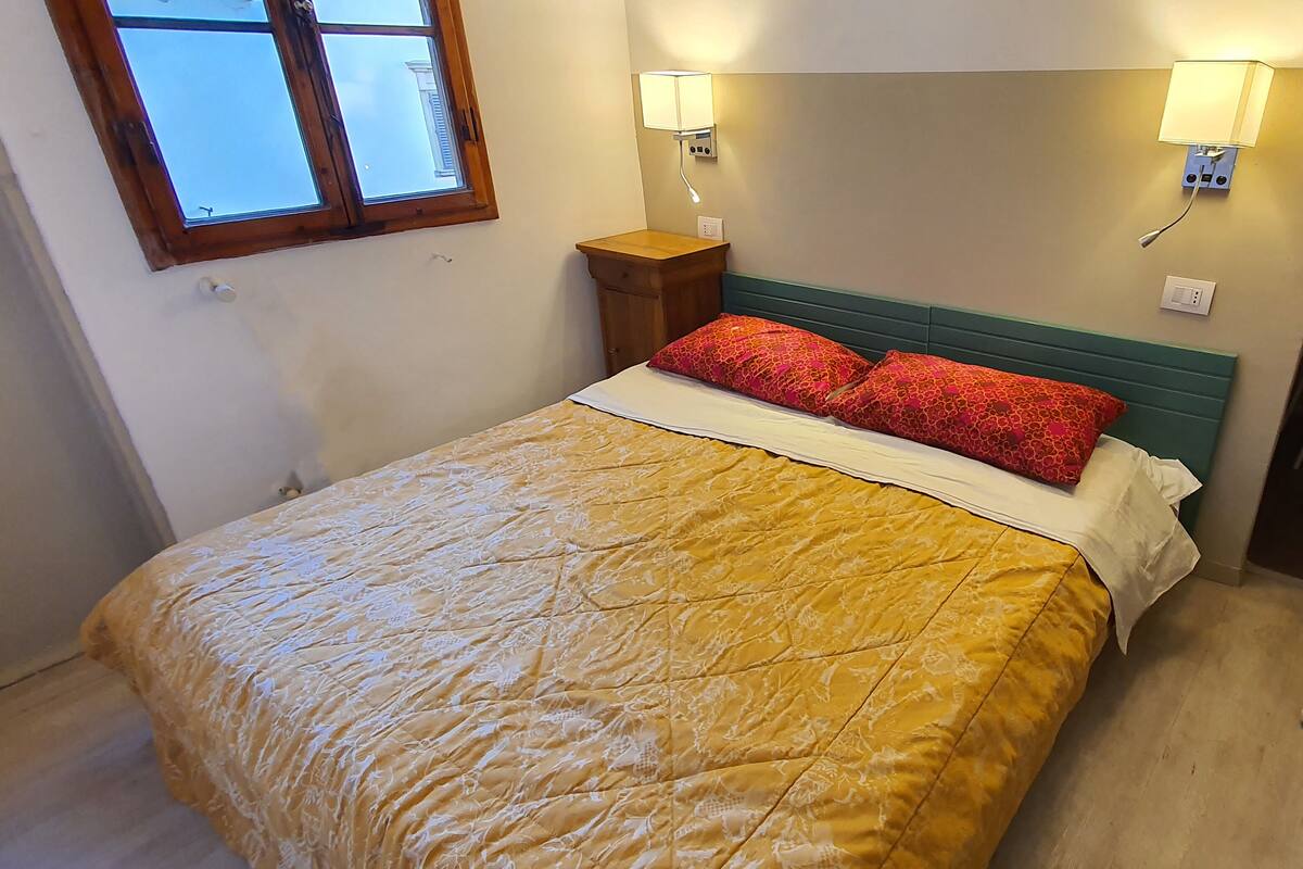A bed with a yellow quilt, two red pillows, and a wooden nightstand with a lamp.