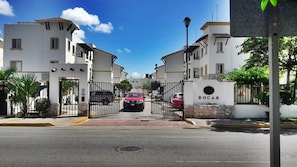 Una entrada cerrada a una zona residencial con edificios blancos, un farol y un cartel que dice 'ROCAR'.