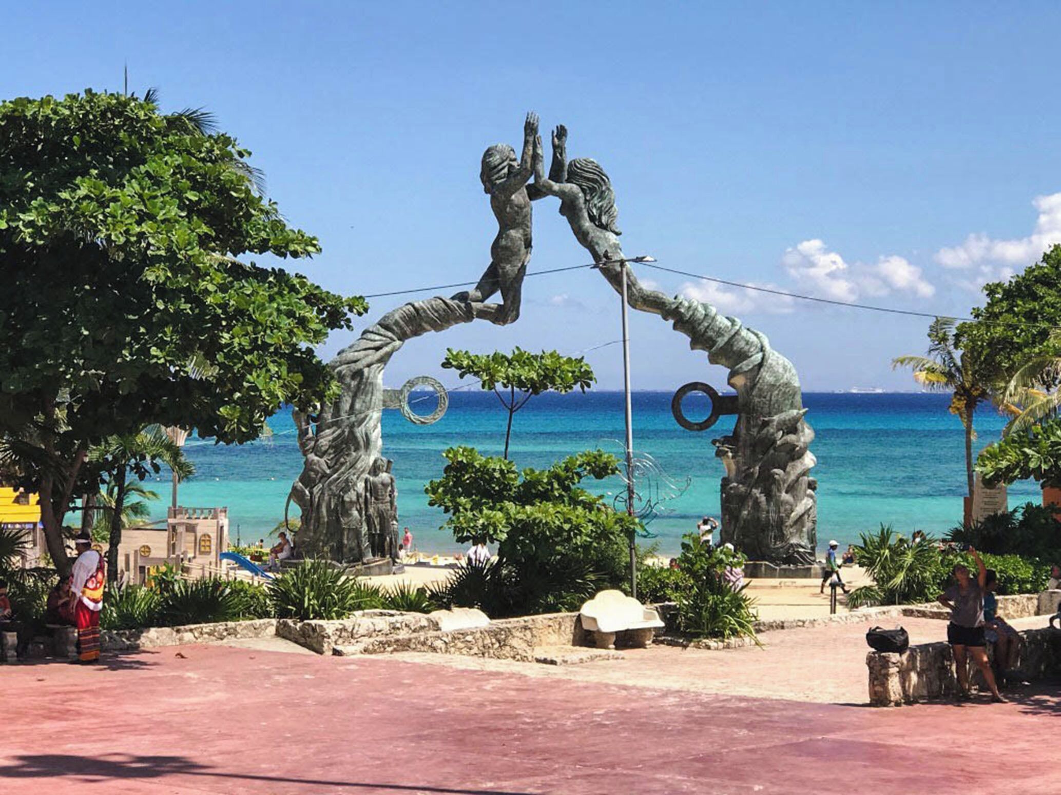 Un arco con estatua y motivo circular, con vistas a una playa y aguas azules cristalinas.